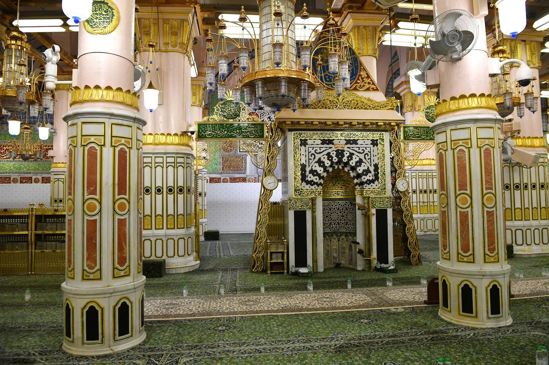 Al-Rawdah inside the Prophet's Mosque in Madinah, with white and gold columns, the mihrab and green carpet